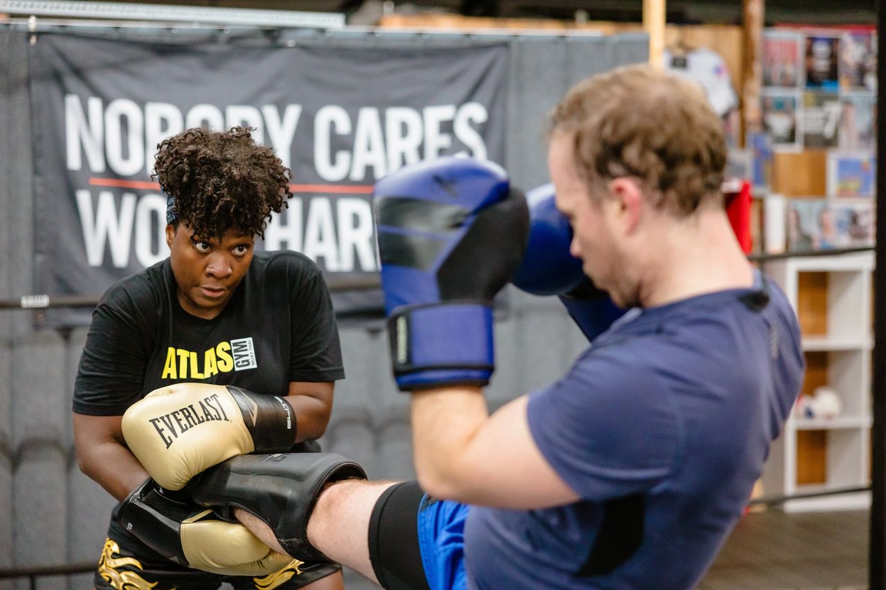 Two Muay Thai students practicing a kick with Thai pads